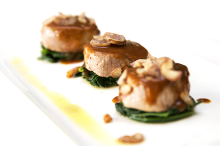lateral shot of three veal fillet medallions with white wine sauce and boiled chestnuts on spinach leafs on white backgroundの写真素材