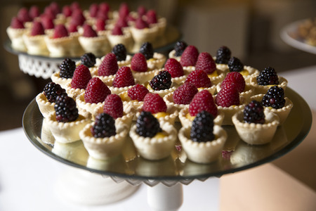 closeup of a wedding buffet, a mirror tray with little short pastry basket filled with custard and with a rasperry and blackberries on itの写真素材