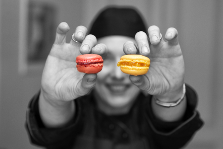 black and white capture with coloured details,  a woman holding two macarones toward the cameraの写真素材