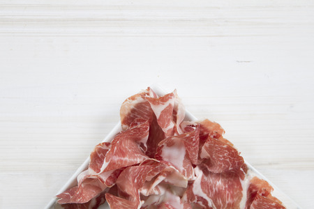 closeup of a square white plate with coppa made in Piacenza (north italy)  in it on a white wooden tableの写真素材