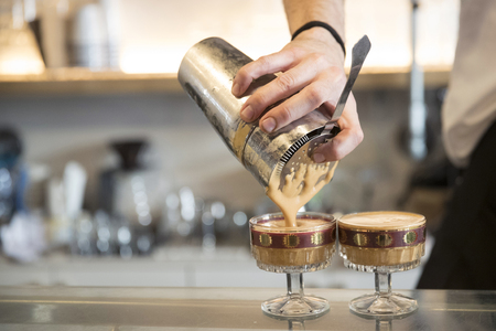 closeup of a barman making two cold shakared coffee on a bar counter, he is pouring coffee into two vintage glasses. Subject and focus on the rightの写真素材