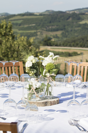vertical shot of a wedding table setting with flowers  vases and seating for guests. Behind the table a beautiful view on the italian hills in Alba, Piemonte at sunset.の写真素材