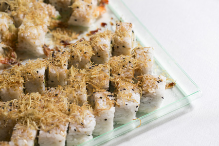 closeup of a tray of salmon uramaki filled with salmon, avocado and fresh cream cheese and garnished with fried onions with focus and subject on the leftの写真素材