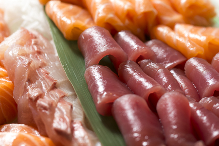 closeup of a tray of salmon, tuna and yellowtail fish sashimi on a leek leafの写真素材