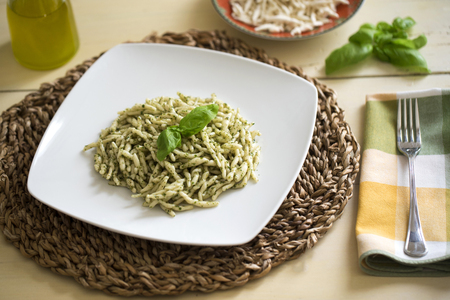 a plate of typical italian pasta with basilicum sauce on a table with basil, olive oil and basilicum leafsの写真素材
