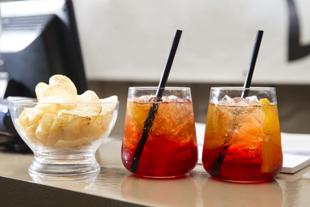 Horizontal shot of a bar counter with Two glasses of colourfull spritz with some chips on it.の写真素材