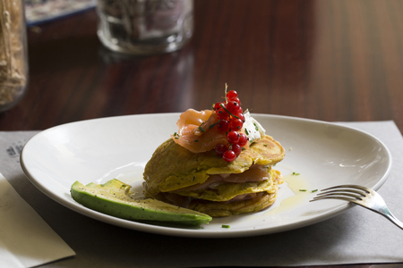 a plate of green pancakes with fresh salmon and slices of avocado on a wooden tableの写真素材
