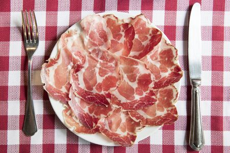top view of a plate of coppa piacentina ( seasoned coppa made in Piacenza north italy) on a red and...