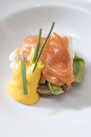 vertical shot of a plate of egg benedict with salmon and dutch sauce decorated with chives, subject and focus on the leftの写真素材