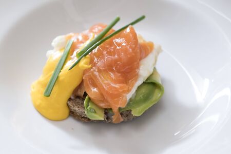 closeup of a plate of egg benedict with salmon, avocado and dutch sauce decorated with chives, subject and focus on the leftの写真素材