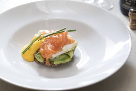 horizontal shot of a plate of egg benedict with salmon and dutch sauce decorated with chives, subject and focus on the leftの写真素材