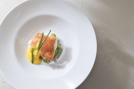 top view of a plate of egg benedict with salmon, avocado slices,  and dutch sauce decorated with chives, subject and focus on the left
の写真素材