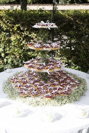 vertical shot of a wedding cake with hearth shaped cupcakes,  cream and fresh raspberries and flowersの写真素材