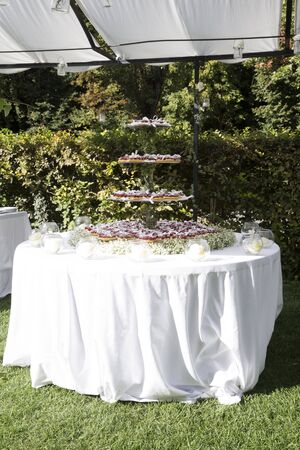 outdoor vertical shot of a round table with a wedding cake on top, the cake is made with hearth shaped cupcakes,  cream and fresh raspberries and flowersの写真素材