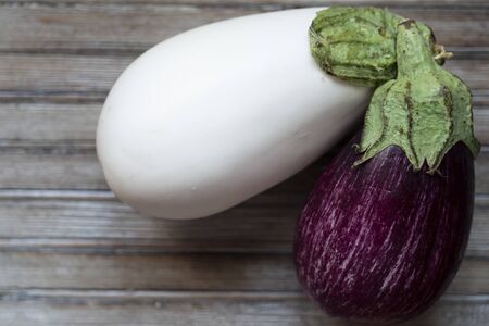 top shot closeup of one white aubergine next to a violet one on a wooden chopboardの写真素材