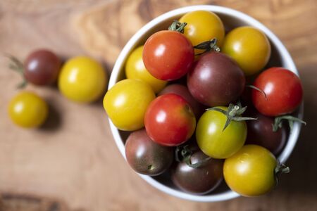 top view shot of a cup full of round and colored little tomatoes on a wooden chopboard.の写真素材