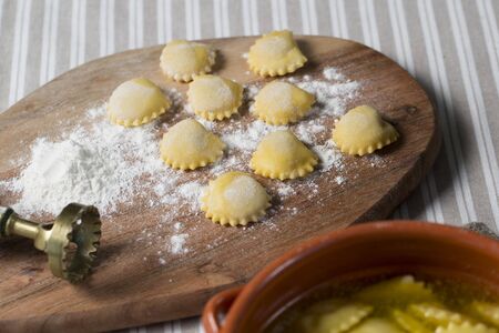 raw Anolini, a typical filled pasta of Piacenza, north italy, on a wooden chop board next to the stencil.の写真素材