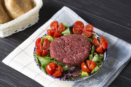 horizontal shot of a plate with a raw hamburger on it on a lettuce and tomatoes salad.の写真素材
