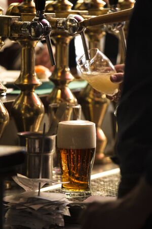vertical closeup of a bartender pouring a dark beer in tap with subject and focus on the rightの写真素材