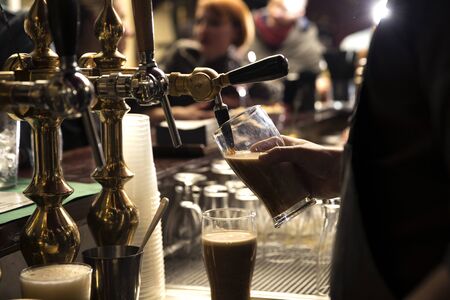 closeup of a bartender pouring a dark beer in tap behind the bar counterの写真素材