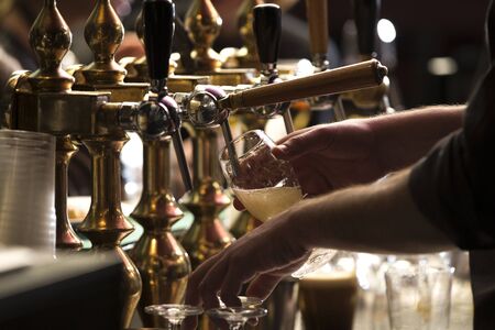 closeup of a bartender pouring a blonde double malt beer in tap behind the bar counterの写真素材
