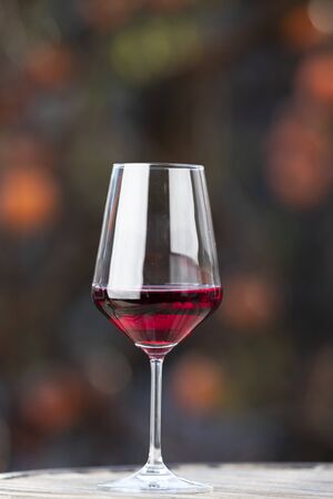 outdoor vertical shot of a glass of red wine with a khaki tree behind at sunsetの写真素材