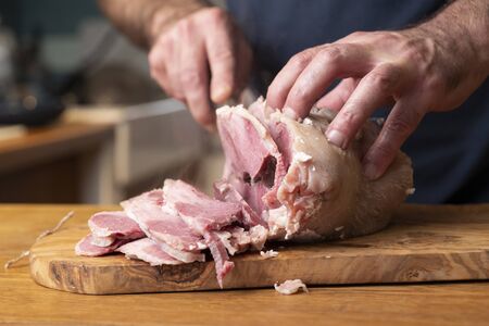 Frontal closeup of a man slicing  a typical italian food of Emilia Romagna on a olive wooden chop board, He slices cappello del prete (hat of the priest) , seasoned pork meat, boiled and sliced.の写真素材
