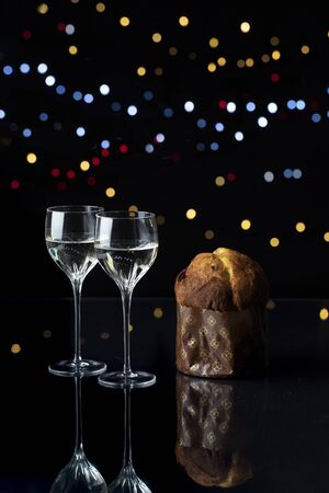 vertical night closeup of two elegant chrystal glasses with an italian panettone on black background with lightsの写真素材