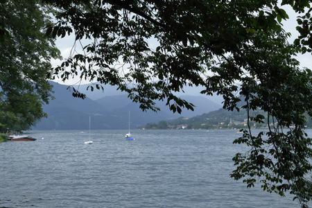 A landscape of Lake Orta, in northern Italy, in a leaves and branches frame, with two sailing boats...
