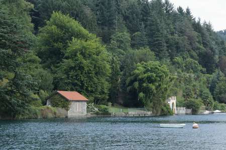 A house with trees next to the lake Orta shore in Novara province, northern Italy, with a boatの写真素材