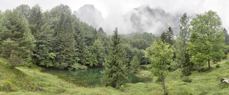 A small green lake in the Montagnole Basse mountains, in the Italian Alps, just after rain, with thick clouds, wet grass and trees.の写真素材