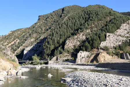 A landscape of Spanish Aragonese Pyrenees, with forest, mountains and an old wooden bridge which leads to Janovas, an abandoned town due to the construction of a dam. The river is Rio Ara.の写真素材