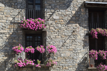 A front view of a stone facade with four black iron railing balconies with violet hanging flower on...