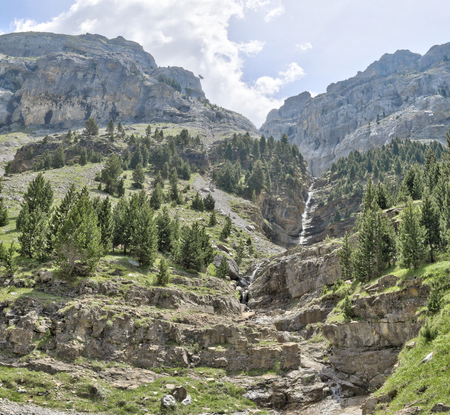 A landscape of a waterfall on mountains surrounded by a pine and firs forest and a deep blue sky with some clouds in Ordesa valley (Valle de Ordesa) national park, as seen from the Hunters' Path (Senda de los Cazadores), in Aragon, Spainの写真素材
