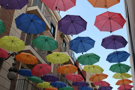 The sun shelter of an open air street through a series of coloured opened umbrellas hanged on cables, with a blue cloudy sky, in Orihuela, Spainの写真素材