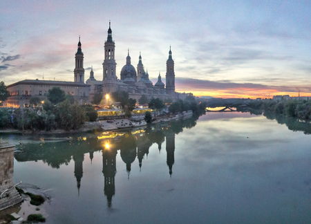 A landscape of Pilar Cathedral and Santiago Bridge reflecting in the Ebro river at sunset, after a storm, in a cloudy autumn, in Zaragoza, Spainの写真素材