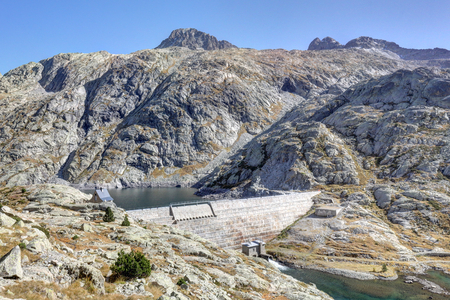 The upper Balchimaña artificial lake with its dam, among barren rocky mountains and a blue sky in a sunny autumn, in Panticosa, Aragon Pyrenees, Spainの写真素材