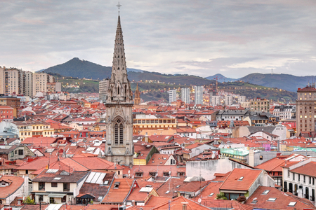 A landscape of Bilbao mountains and city centre with clouds, mountains, houses roofs and the cathedral belltower at sunset, in Vizcaya, Spainの写真素材