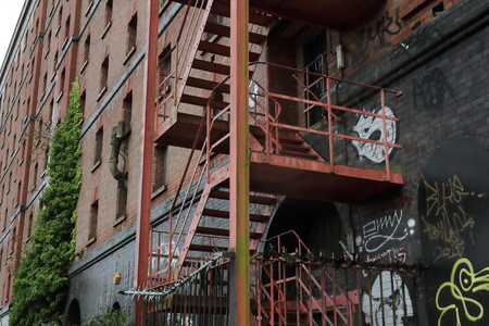 Metal fire escape stairs on an abandoned dark grey and red bricks building with climbing green ivy and graffiti in Bristol, United Kingdomのeditorial素材