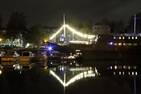 A big sailing boat with fairy lights and decorations reflecting on the Avon river in the Spike Island wharf, by night, United Kingdomのeditorial素材