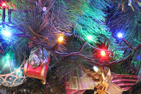 A close view of a green leaves Christmas tree with electric lights decorations, hanging ornaments and baubles in a bright colored atmosphereの写真素材