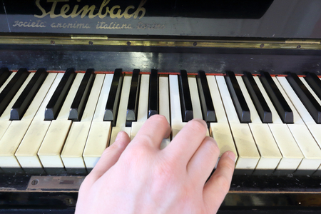 A right hand playing a G (SOL) major chord on an old black piano with yellowed cracked keys, pressing the G (SOL), B (SI), D (RE) notesのeditorial素材
