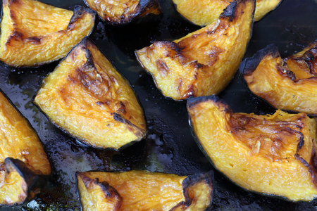 A close view of some orange roasted and crunchy pumpkin slices cooked in an oven over a black glass surface, with black edgesの写真素材