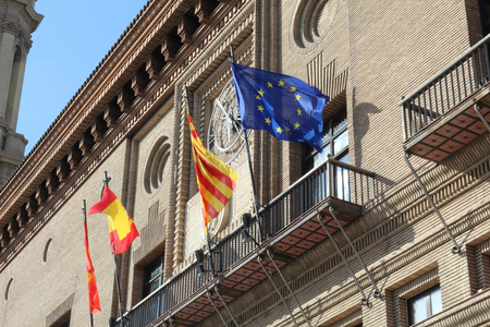 The Zaragoza, Aragonese, Spanish and European flags flapping against a blue sky om font of the city hall during a sunny summer day in Zaragoza, Spainのeditorial素材