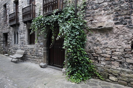 A wooden door with green ivy on a stone made house with some wooden balconies in the rural Pyrenees...