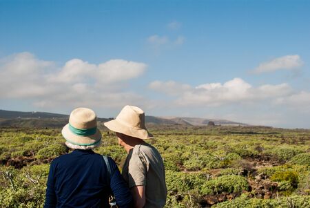 senior tourist couple with hat on their backs in a green landscape