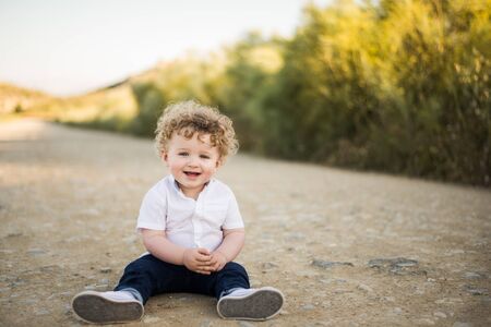 smiling blond boy sitting on the road in summerの写真素材