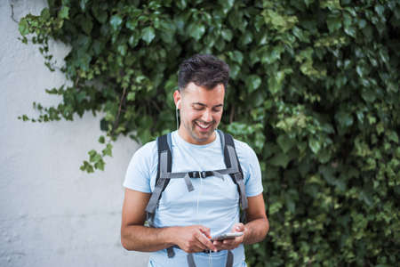 young smiling sportsman standing outside typing something on his smart phone