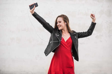 Positive happy blonde girl with a wide smile listening to music on her smart phone.の写真素材