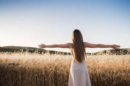 Young woman on her back opens her arms in the field feeling free